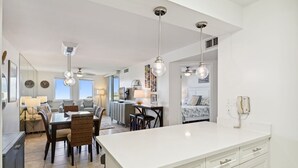 A modern kitchen with a central island, a dining area with a table and chairs, and a living space with a sofa and a TV. - Sunset Jetty View! Enjoy one free beach chair set up and umbrella each day! (Destin)