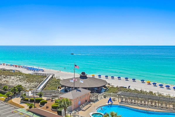 A beachside resort with a pool, beach umbrellas, and a flag.
