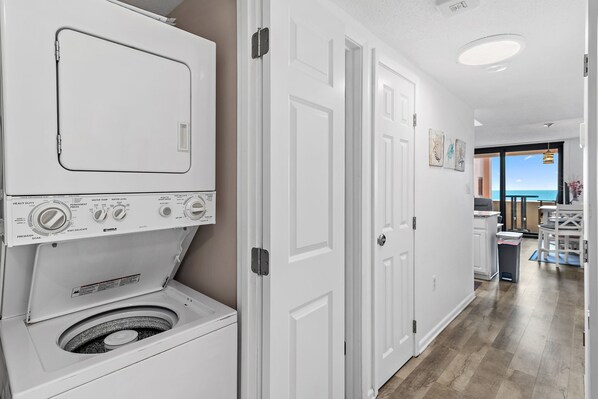 A laundry area with stacked washer and dryer, a white door, and a view of the ocean through a glass door.