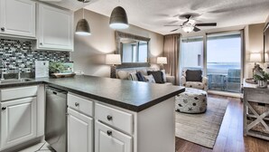 A modern kitchen with white cabinets, a black countertop, and a large island. There is a dining area with a view of the ocean.