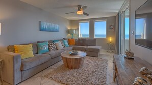 A living room with a grey sofa, a round coffee table, and a ceiling fan. - Fabulous sunset Jetty view! Enjoy one free beach chair setup each day! (Destin)