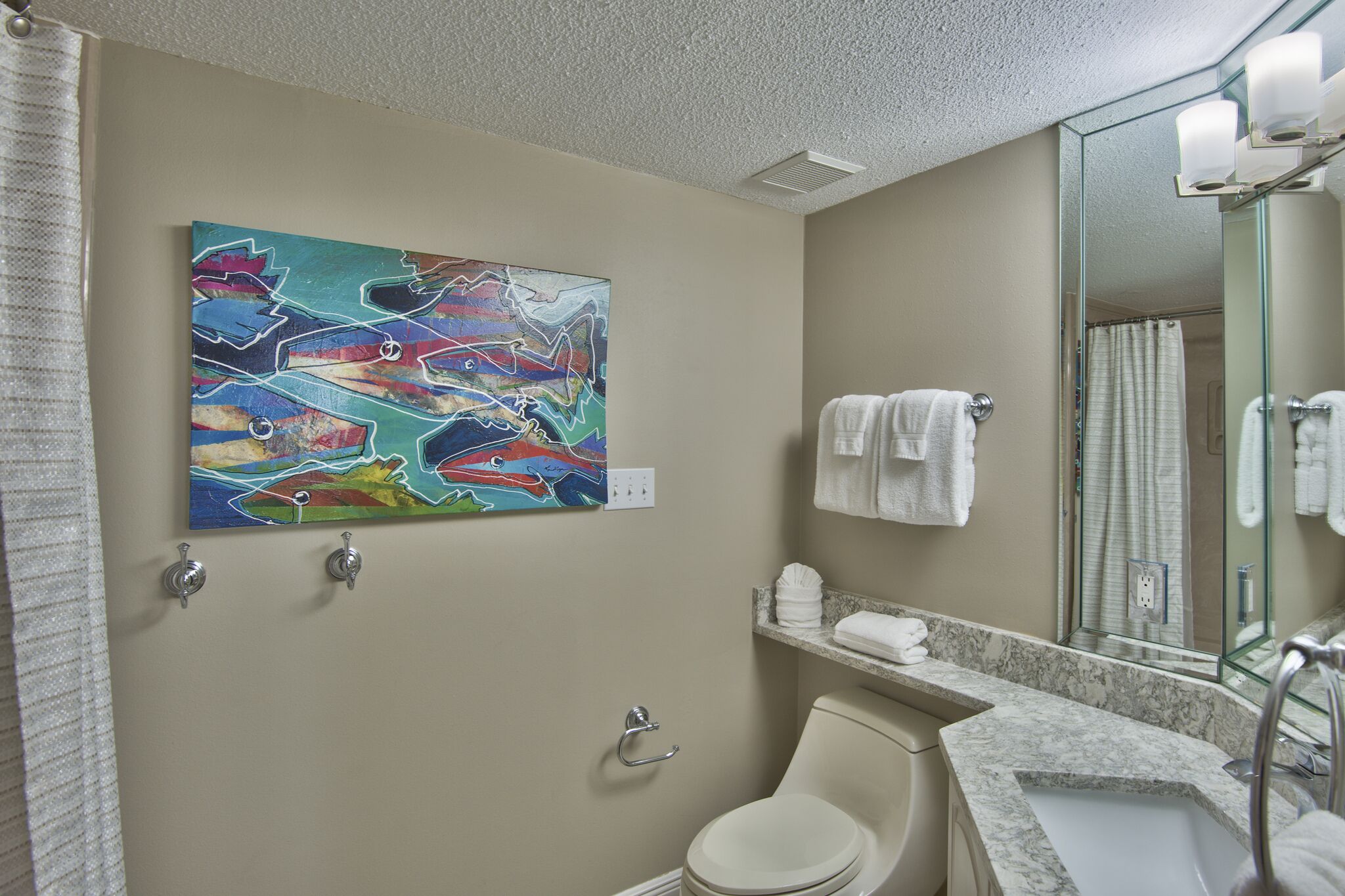 A bathroom with a marble sink, a toilet, a mirror, and a colorful abstract painting on the wall.