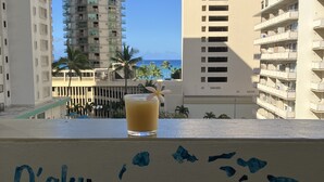 Un verre posé sur un balcon, avec vue sur un grand immeuble et des palmiers.