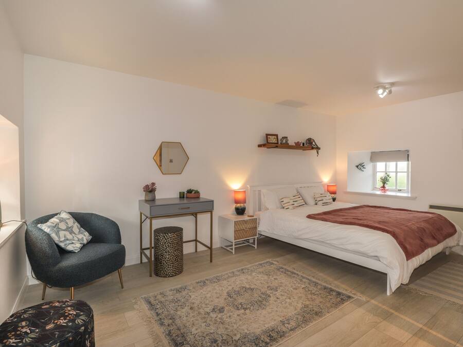 Une chambre à coucher comprenant un lit, un bureau, une chaise, une petite table, un tapis et une fenêtre.