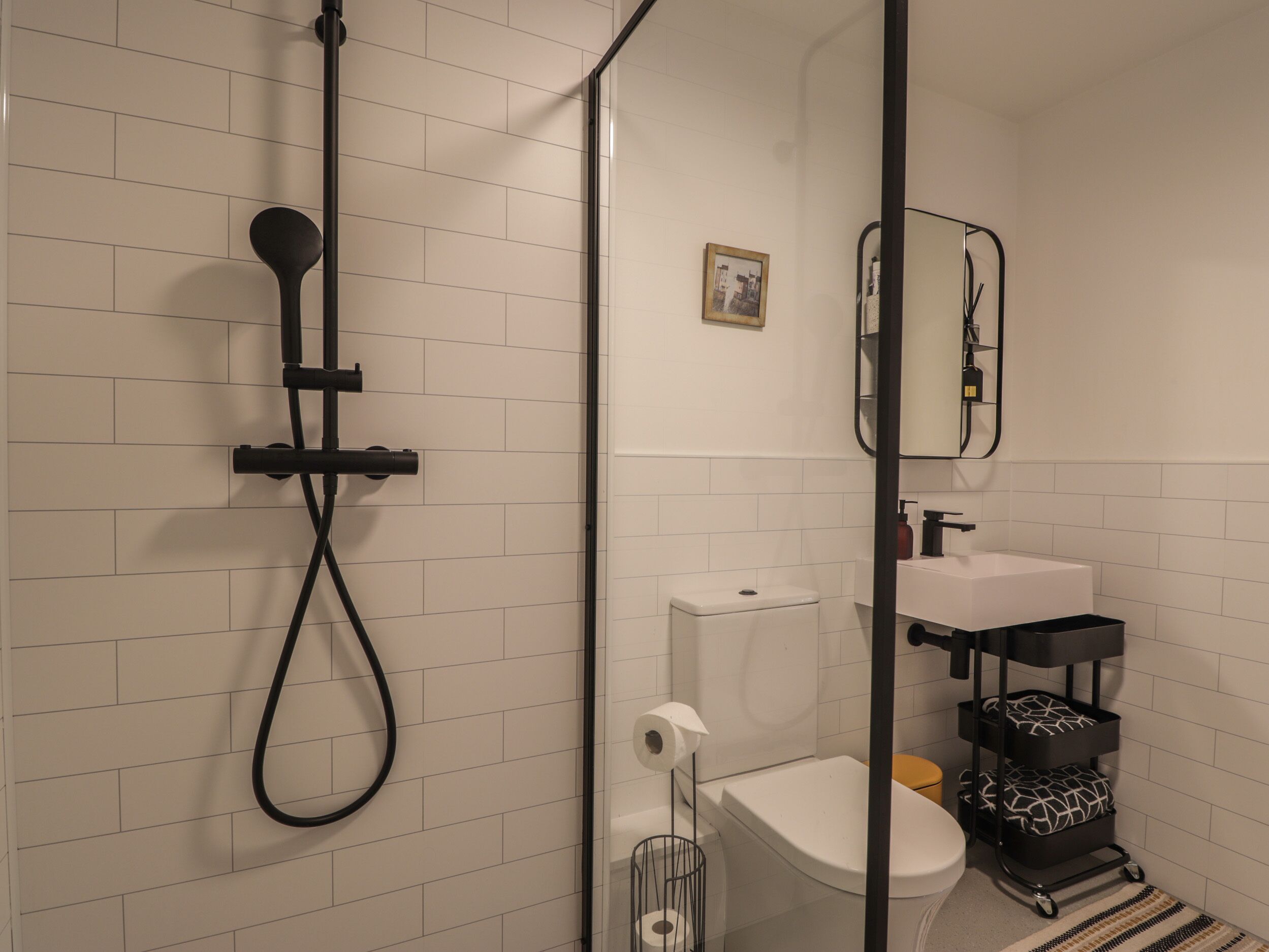 Une salle de bain moderne avec une douche à parois de verre, des toilettes, un lavabo et un meuble de rangement noir sur roulettes.