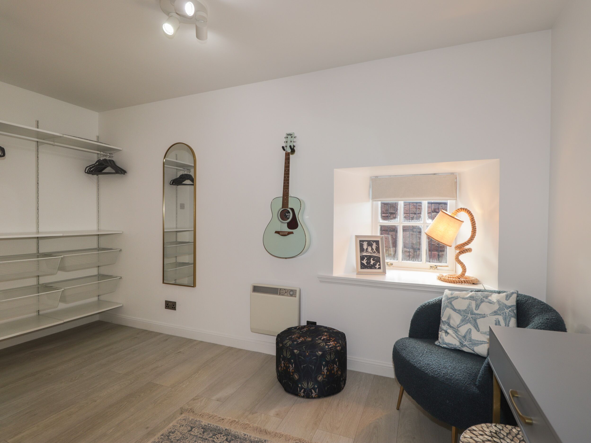 Una habitación con una guitarra, un espejo, una lámpara y una silla.
