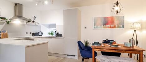 A modern kitchen with white cabinetry, a central island, and a dining area with a wooden table and blue chairs.