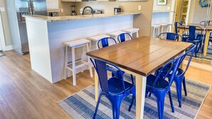 A modern kitchen with a central island, white bar stools, and blue chairs around a wooden dining table. - L👀K! NEW VRBO! Beach & Lake; Boat Ramp; Lake Powell! Rent both sides, sleeps 18 (Panama City Beach)