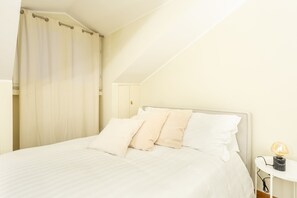 Quarto com cama, almofadas, mesa de cabeceira e abajur.
