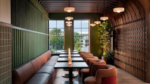 A modern interior with a long bench seating area, tables, and pendant lighting. - Ada Hotel (Ada)