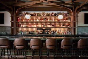 A bar area with a wooden ceiling, multiple shelves of liquor bottles, and four bar stools. - Ada Hotel (Ada)