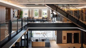 A modern hotel lobby with a reception desk, seating area, and a staircase. - Ada Hotel (Ada)