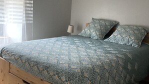 A bedroom with a wooden bed frame, a patterned bedspread, and a nightstand with a lamp. - Gîte Charmant Dans Maison Ardéchoise au Coeur des Montagnes Pour Amoureux Nature (Saint-Michel-de-Chabrillanoux)