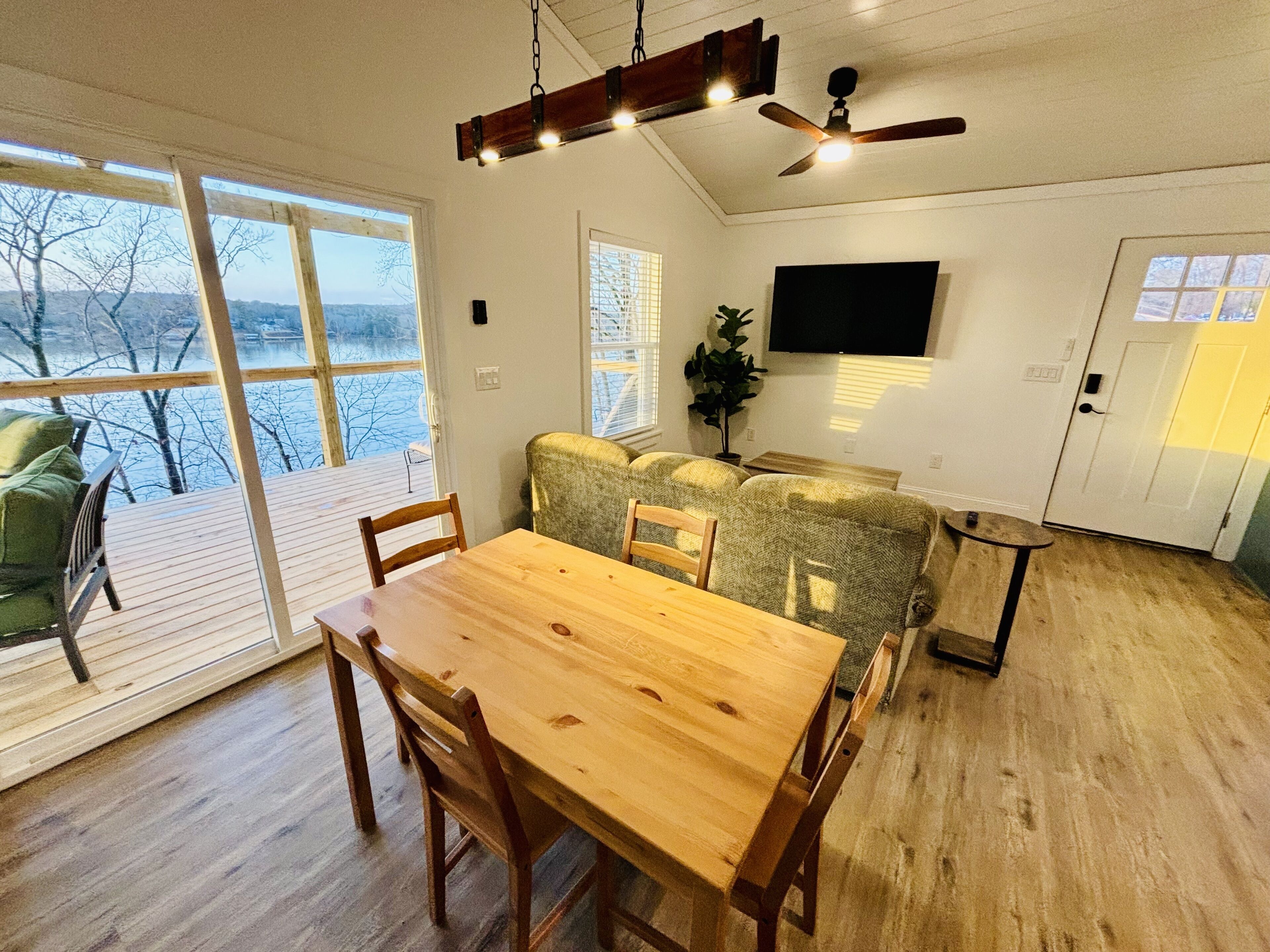 A cozy room with a wooden dining table, chairs, a sofa, and a TV mounted on the wall.