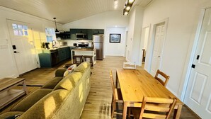 Ein gemütliches Wohnzimmer mit einem Holzesstisch und Stühlen, einer Couch und einer Küche im Hintergrund.