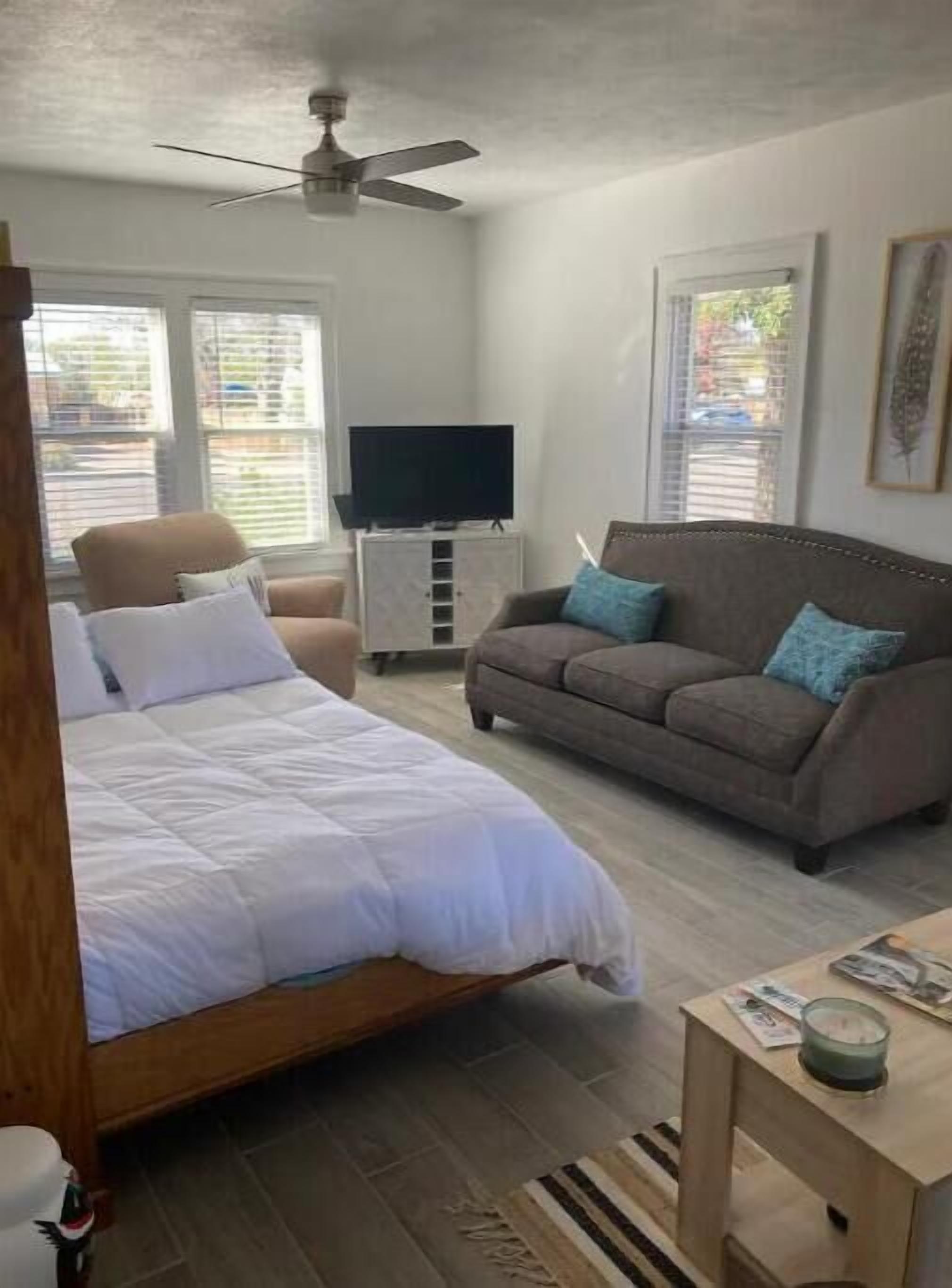 A bedroom with a bed, a sofa, a television, and a ceiling fan.