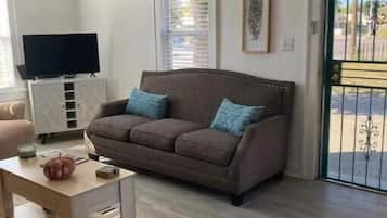 A living room with a brown sofa, a wooden coffee table, a television on a cabinet, and a door with a metal gate.