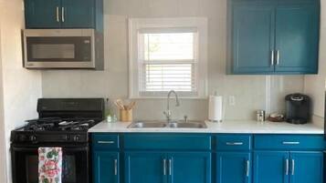 A kitchen with teal cabinets, a black stove, a microwave, a sink, and a window with blinds.