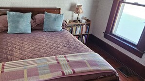Un letto con copriletto trapuntato, due cuscini, un comodino con una lampada e una libreria.