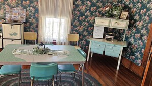 Una cucina d'epoca con un tavolo verde, sedie color petrolio e carta da parati floreale.