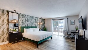 Een moderne slaapkamer met een bekleed bed in groene stof, een houten vloer, een bureau met stoel en een groot raam met uitzicht op het landschap.