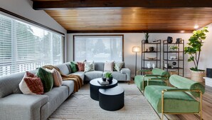 Een moderne woonkamer met een modulaire bank, een ronde salontafel en een groene fauteuil. Er is een boekenkast en een potplant.