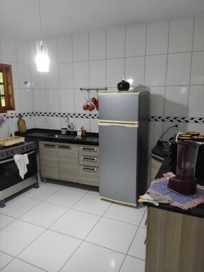 Une cuisine avec des murs recouverts de carreaux blancs, un réfrigérateur noir, une cuisinière et un mixeur posés sur le plan de travail.