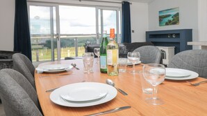 A dining area with a table set for four, a bottle of wine, and a scenic view through large windows. - Buttercup Lodge (Dartmouth)
