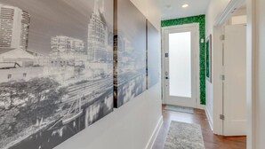 A hallway with a cityscape mural, a green accent wall, and a door with a window. - Prime Nashville Getaway – Peaceful Area (Nashville)