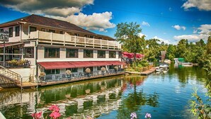 A riverside building with a balcony, a dock, and a row of outdoor seating. - Woodpecker, Spa,Foyer,Bike,Ski! (Orford)