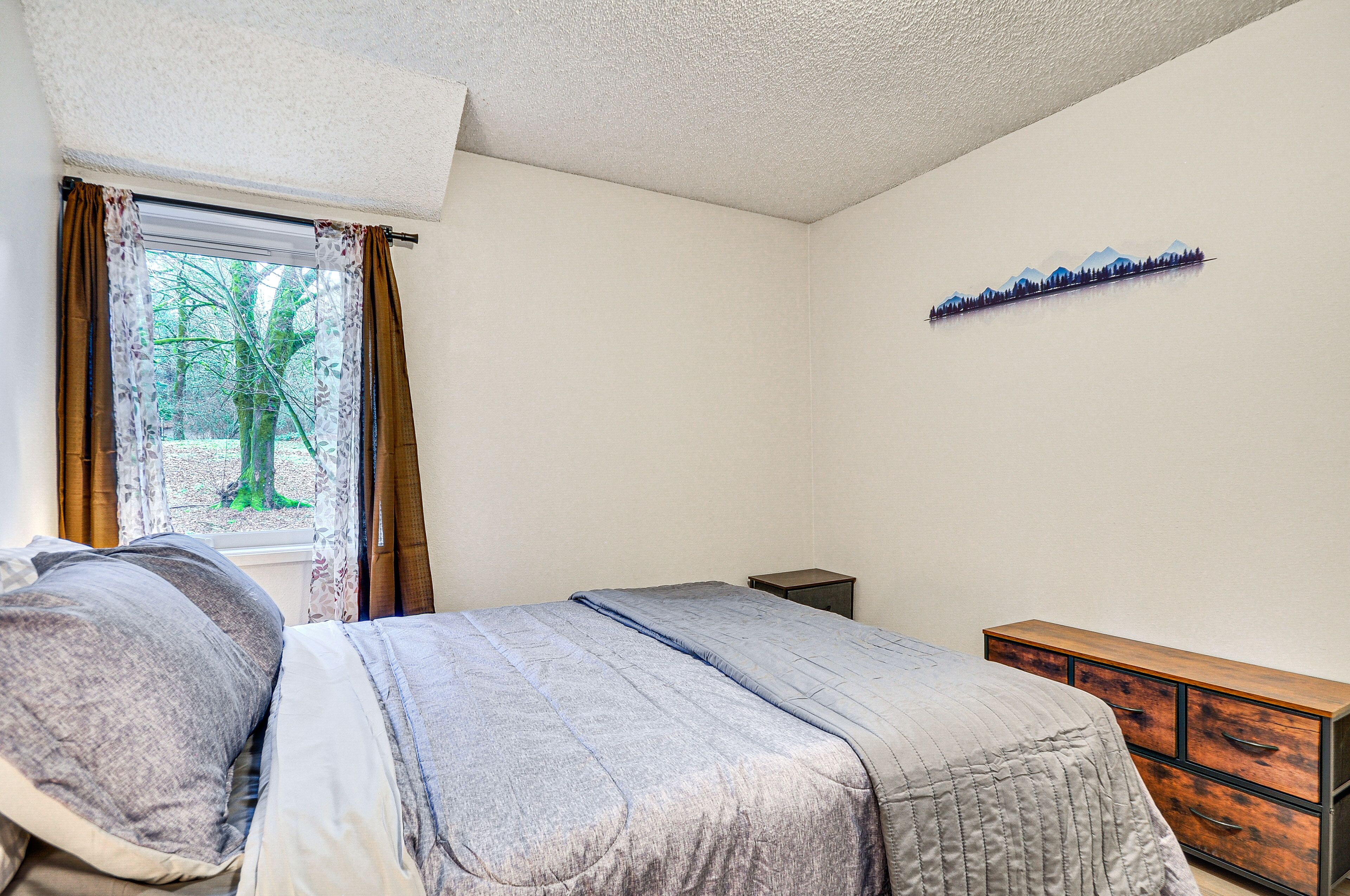 A bedroom with a bed, a dresser, and a window with curtains.
