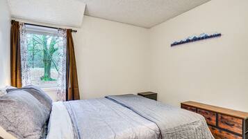 A bedroom with a bed, a dresser, and a window with curtains.