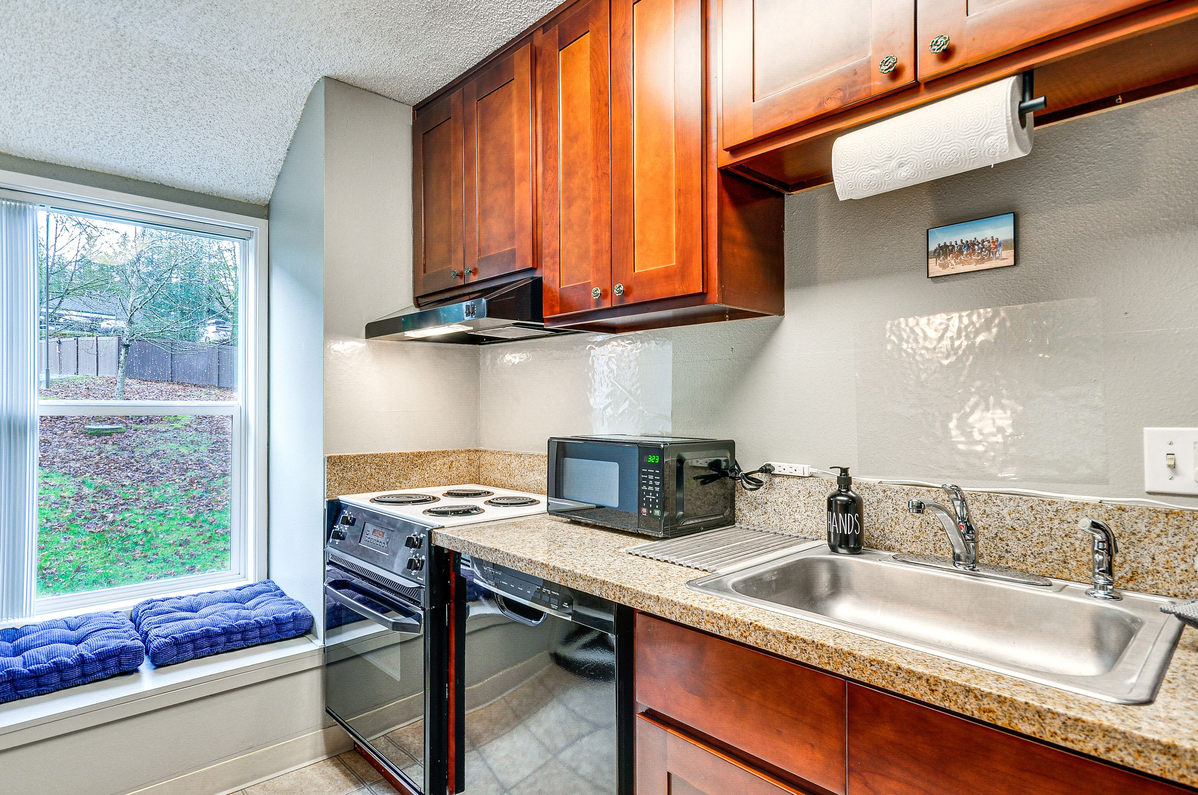 A kitchen with wooden cabinets, a stainless steel sink, a microwave, and a stove.