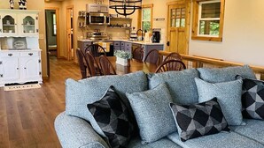 Una sala de estar amplia con un sofá gris, una zona de comedor con sillas de madera y una cocina con electrodomésticos modernos.