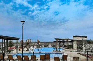 Un área de piscina con sillas de descanso, un espacio de estar cubierto y cielo despejado.