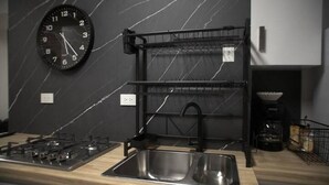 A modern kitchen with a black marble backsplash, a stainless steel sink, a gas stove, a black clock, and a black hanging rack. - Luxurious apartment near the consulate.

 (Juárez)