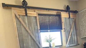 Ein Essbereich mit einem Holztisch und vier Stühlen. Über dem Tisch befindet sich ein Fenster mit Holzläden, und ein Blumentopf steht auf der Fensterbank.
