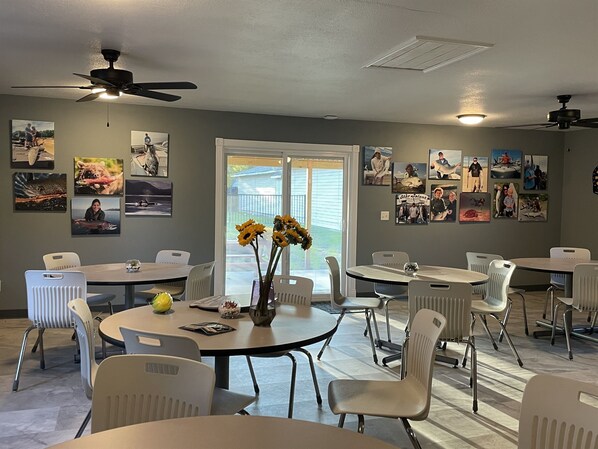 A conference room with round tables and white chairs, decorated with framed photos and a vase of sunflowers.