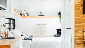 Een compacte, moderne slaapkamer met een bed, witte kasten, een houten bureau en een kleine keukenhoek.