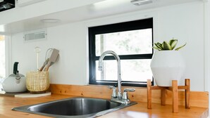 Een keuken met een roestvrijstalen spoelbak, een houten aanrechtblad en een raam met uitzicht op groen.