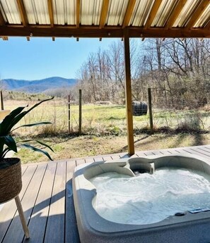 Un bain à remous sous une pergola en bois, avec vue sur un champ verdoyant et des montagnes en arrière-plan.