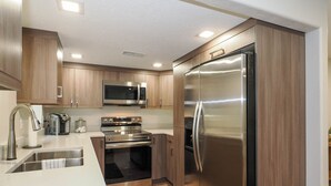 A modern kitchen with stainless steel appliances, wooden cabinets, and a white countertop. - Cozy, Quiet East Bench Basement Apartment  (Sandy)