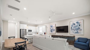 A modern living room with a sofa, a dining table with chairs, a TV, and artwork on the wall.
