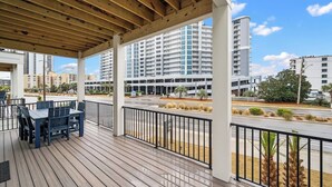 A covered outdoor area with a wooden deck, a table with chairs, and a view of high-rise buildings in the background.