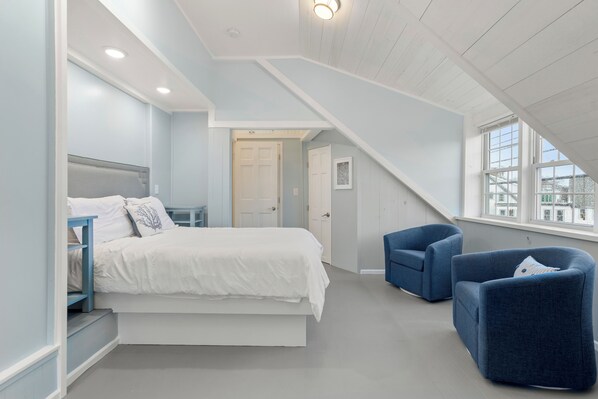 A bedroom with a bed, nightstands, a desk, two armchairs, and a window with a view. - 2BR/2BA Harborside Home · Fenced Backyard · Ocean View ·Walk to Rocky Neck+Beach (Gloucester)
