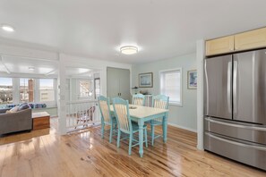 A modern kitchen with a dining area, wooden floors, and a large stainless steel refrigerator. - 2BR/2BA Harborside Home · Fenced Backyard · Ocean View ·Walk to Rocky Neck+Beach (Gloucester)