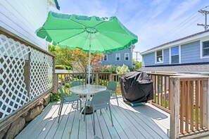 A deck with a table and chairs, a green umbrella, and a barbecue grill. - 2BR/2BA Harborside Home · Fenced Backyard · Ocean View ·Walk to Rocky Neck+Beach (Gloucester)