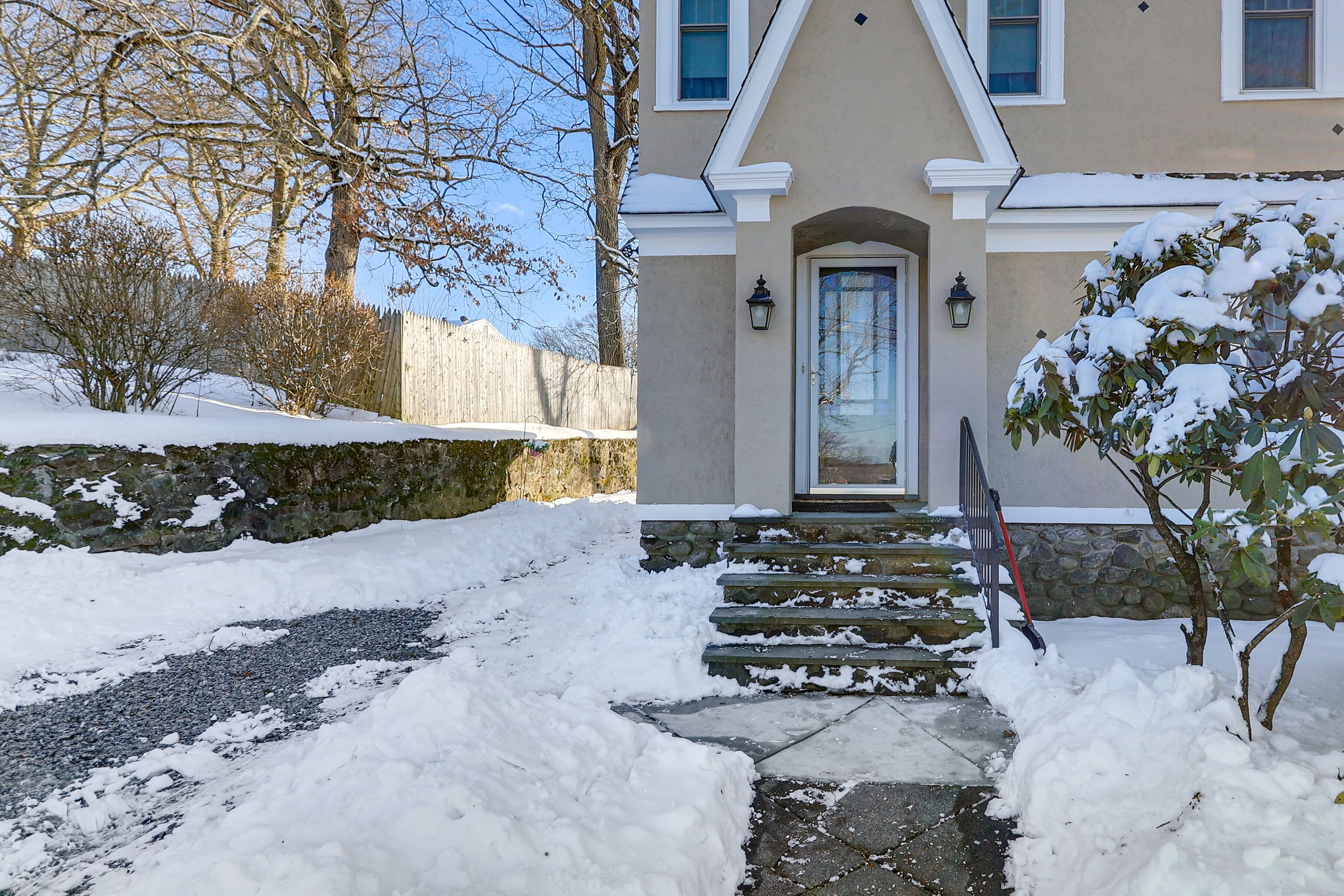 A snow-covered pathway leading to a house with a stone staircase and a door.