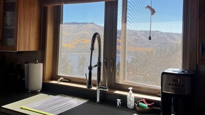 Una cocina con armarios de madera, un lavamanos de acero inoxidable, un ventanal con vistas a las montañas y una lámpara colgante.