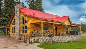 Eine Blockhütte mit Stein Fundament, rotem Dach und einer Veranda.